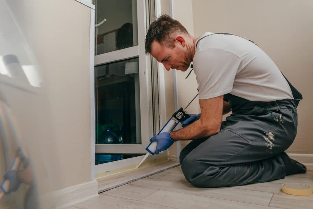 Young man applying sealing to door to prevent water damage